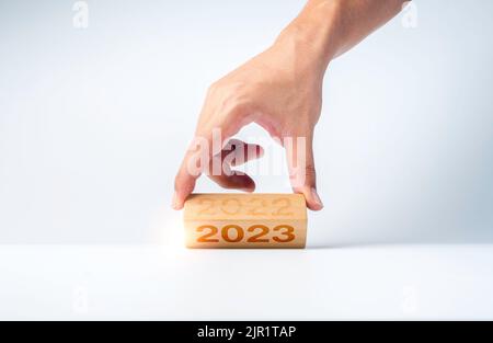 Nahaufnahme Hand Umblättern der 2022 bis 2023 Jahre Zahlen Kalender auf Holzwürfelblöcke für die Vorbereitung der neuen Jahr ändern, beginnen und neue Geschäfte zu starten Stockfoto