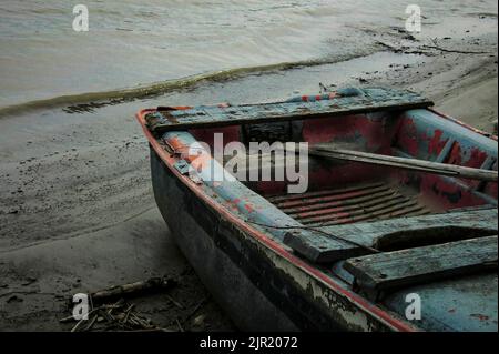 Kleines Holzboot zerstört und getragen von Zeit und Wetter verlassen an den Ufern eines Flusses in Italien. Stockfoto