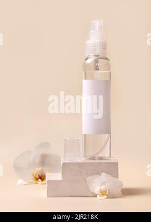 Sprühen Sie die Dispenser-Flasche in der Nähe von weißen Orchideenblumen und beigen Steinen auf hellbeige Nahaufnahme, Mockup. Hautpflege Beauty-Produkt-Paket. Naturkosmetik, Stockfoto