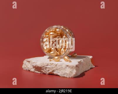 Gesicht Serumkapseln in einem Glas auf Travertin-Steinen auf roten Nahaufnahme. Hautpflege Beauty-Produkt. Gesichtskosmetik, minimale Pastellzusammensetzung Stockfoto