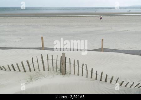 West Wittering, Großbritannien, 21. August 2022: Sand stapelt sich am Fuße der Sanddünen von West Wittering und überwältigt einen alten Holzzaun. Neueres Kunststoffgewebe Stockfoto