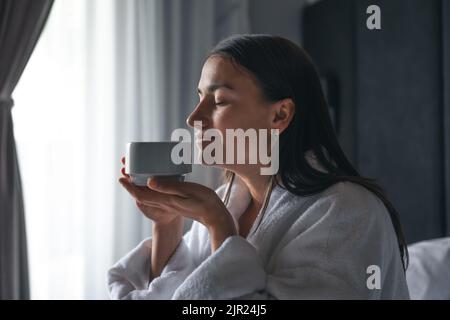 Eine junge Frau mit einer Tasse Kaffee im Bett. Stockfoto