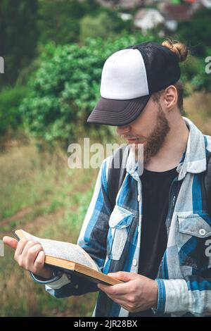 Ein Mann in einem karierten Hemd liest in der Natur ein Buch. Stockfoto
