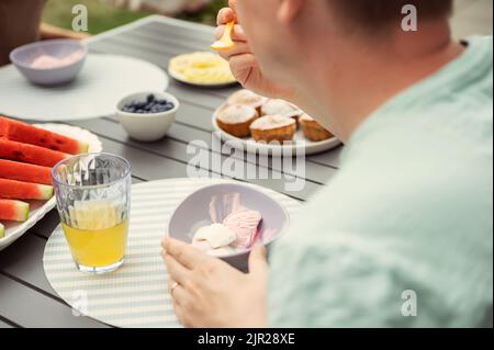 Junger Mann, der im Café im Freien Eis und Süßigkeiten isst. Blick von hinten Stockfoto