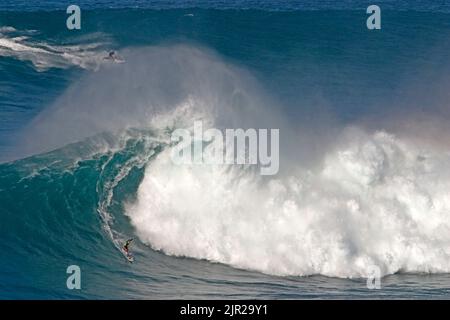 Ein Surfer kommt zum Ende seines hawaiianischen Big Surf Ride, während sein Mitläufer zur nächsten Welle fährt, um ihn in Peahi (Jaws) vor Maui abzuholen. Stockfoto