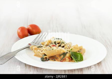 Leckere glutenfreie Pasta-Nudeln auf weißem Teller mit Tomaten und Käse und Basilikum in cremiger Sauce mit Gabel Stockfoto