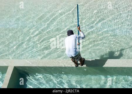 Rückansicht von oben aufgenommen, als ein Wartungsarbeiter in Mexiko einen Pool mit einer Bürste reinigte Stockfoto