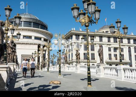 Die Kunstbrücke über den Fluss Vandar mit dem Finanzpolizeiamt und dem Gebäude des Außenministeriums im Hintergrund.Skopje, Nordmakedonien. Stockfoto