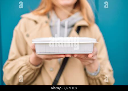 Frau Hände halten leere weiße Kunststoff Einweg-Lebensmittelbehälter Modell mit Kopie Platz auf blauem Hintergrund. Lieferungslebensmittelkonzept. Stockfoto