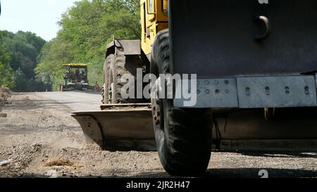 Straßenbauarbeiten, Reparatur einer Autobahn, der Traktor nivelliert Kies auf der Straße, so dass eine Basis für die Verlegung des Asphalts. Hochwertige Fotos Stockfoto