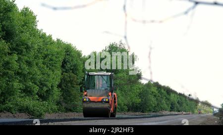 Straßenbau arbeitet mit Walzenverdichter Maschine und Asphalt Finisher. Straßenwalze, die während des Straßenbaus frischen Asphalt auf den Kiesboden legt. Hochwertige Fotos Stockfoto