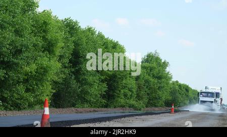 Reparatur einer Autobahn, spezielle Bewässerungsmaschine besprüht Wasser auf neuen frischen Asphaltbelag, Abdeckung auf einer Seite des Verkehrs. Straßenbauarbeiten. Hochwertige Fotos Stockfoto