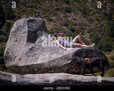 Hundebesitzerin ruht auf einem Granitfelsen mit Sofaform und Schokolade labrador Retriever. Stockfoto