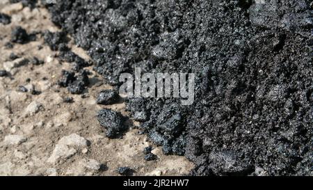 Nahaufnahme, frischer Asphalt im Prozess der Verlegung auf der Straße, große Klumpen, in Harz, schwarz, scheint in der Sonne,. Hochwertige Fotos Stockfoto