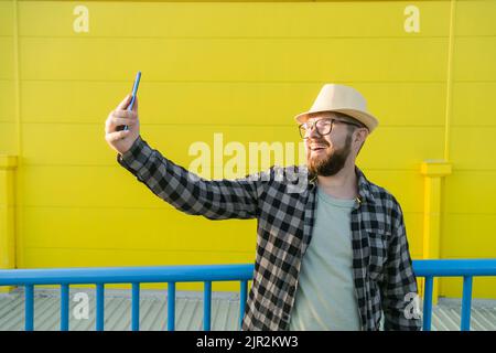 Mann, der etwas an der Kamera erzählt, während er in der neuen Stadt unterwegs ist, gelber Supermarkt-Hintergrund. Blogger- und vlog-Konzept Stockfoto