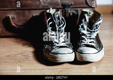 Gebrauchte alte Sneakers mit Vintage-Koffer im Hintergrund Stockfoto