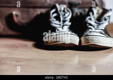 Alte Sneakers mit Vintage-Koffer im Hintergrund Stockfoto