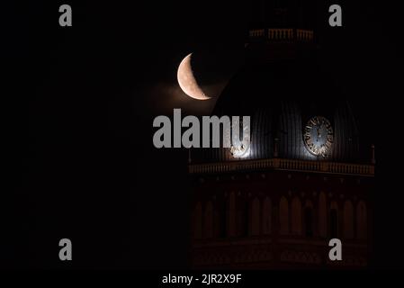 Wunderschöner Viertelmond über der Altstadt von Riga hinter der Domes-Domuhr. Stockfoto