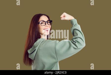 Glücklich lächelnd selbstbewusstes junges Studentenmädchen, das ihren Arm beugte und ihre Kraft zeigte Stockfoto