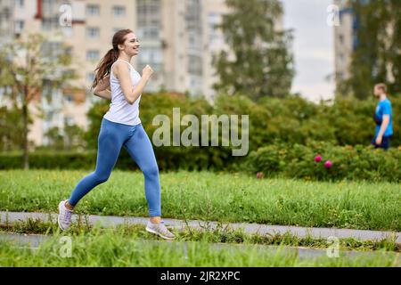 Lächelnde Läuferinnen fahren am Sommermorgen im Parkbereich des Wohngebiets. Stockfoto