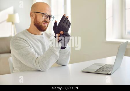 Mann mit rheumatoider Arthritis knetet die Hände, auf denen er spezielle Kompressionshandschuhe trägt. Stockfoto