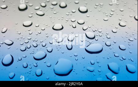 Regentropfen perlend auf einer glatten Glasoberfläche, Blick in den niedrigen Winkel mit geringer Schärfentiefe. Stockfoto