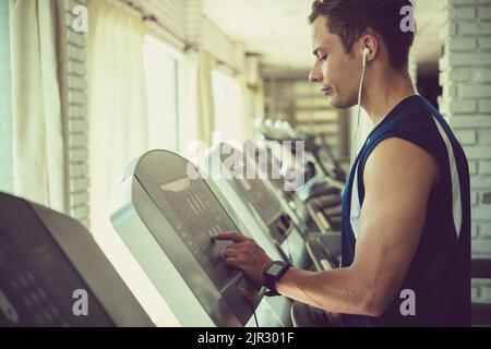Junger sportlicher Mann, der sich für ein Programm auf dem Laufband im Fitnessstudio entscheidet Stockfoto