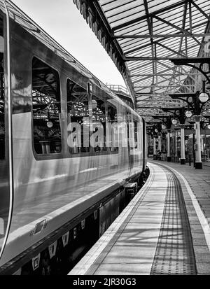 Ein Zug steht neben einem Bahnhofssteig. Ein historisches Baldachin aus dem 19.. Jahrhundert, das von Säulen getragen wird, spiegelt sich auch im Kutschenwindo wider Stockfoto