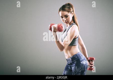 Studioportrait einer hübschen jungen vietnamesischen Frau, die mit Hanteln exersicing Stockfoto