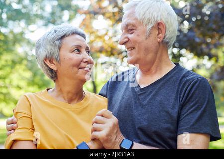 Optimistischer attraktiver multirassischer Geiz Ältere 60s sportliche Paare posieren im Freien, halten Hände lächelnd und blicken einander mit Zärtlichkeit und Liebe an. Ha Stockfoto