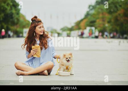 Junge Frau, die auf dem Boden sitzt und mit ihrem Hund zu Mittag gegessen hat Stockfoto