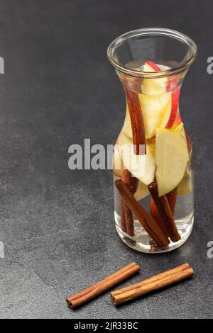 Zimt und Apfel infundiert Wasser in Glasflasche. Zimtstangen auf dem Tisch. Speicherplatz kopieren. Schwarzer Hintergrund. Draufsicht Stockfoto
