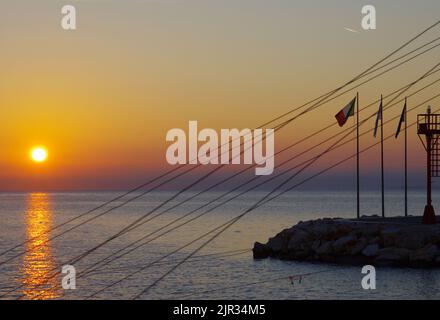 Sonnenaufgang im Hafen von Termoli, im Vordergrund die Silhouette des Leuchtturms und der Flaggen. Molise, Adria Stockfoto