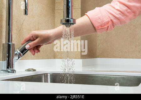 Das Mädchen schließt den Wasserhahn in der Küche, aus der Wasser fließt, als Symbol für die Ressourcenschonung Stockfoto