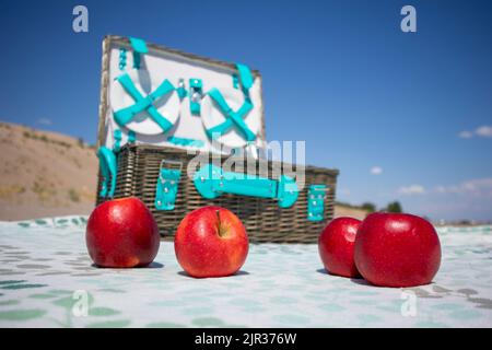 Rote Äpfel auf einer Decke und einem Picknickkorb Stockfoto