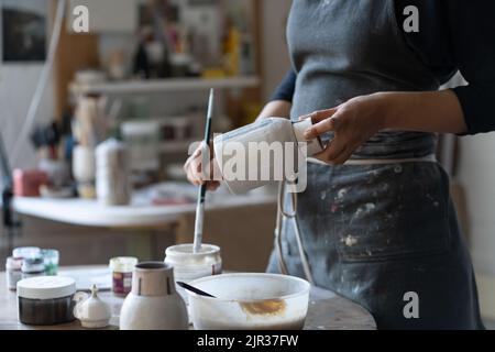 Crop Foto von Frau Handwerker Herstellung Steingut Vase Vorbereitung für die Farbe mit Pinsel Stockfoto