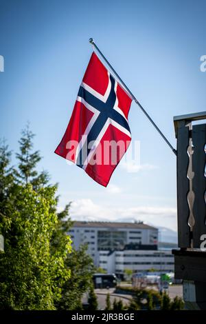 Eine vertikale Aufnahme der norwegischen Flagge, die von einem Balkon mit Gebäuden im Hintergrund hängt Stockfoto