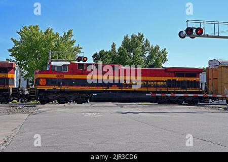 EMPORIA, KANSAS - 13. AUGUST 2022 Kansas City Southern Lokomotiven, die einen langen Zug von Autotransportwagen ziehen, werden an einer Zugkreuzung in der Innenstadt von Emporia angehalten und fahren dann auf ein Abstellgleis, um 3 BSNF-Expresszüge auf den Hauptgleisen nach Osten und Osten ausfahren zu lassen. Stockfoto