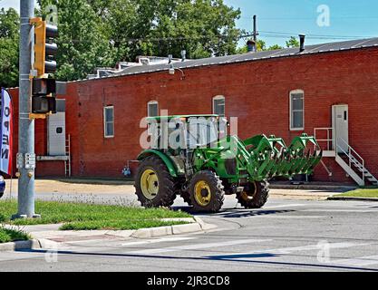 EMPORIA, KANSAS - 13. AUGUST 2022 John Deere Traktor mit Heuballenaufsatz fährt auf der Main Street von einem Betrieb zum anderen, um das Stapeln von Heuballen zu beenden Stockfoto