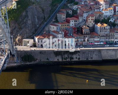 Ribeira-Viertel in Porto, Portugal, mit dem Douro-Fluss und pastellfarbenen Häusern am Flussufer und der Seilbahn links. Stockfoto