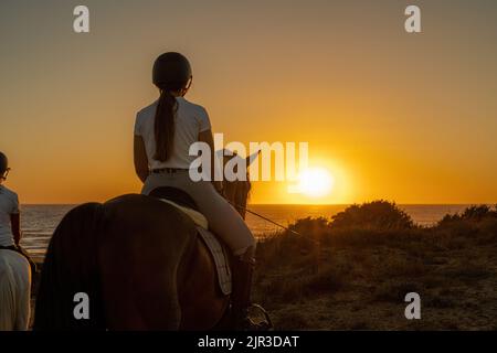 Rückansicht einer jungen Frau auf dem Pferderücken, die den Sonnenuntergang beobachtete. Stockfoto