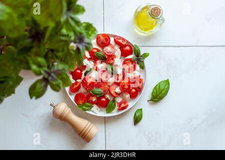 caprese-Salat unter der Basilikumpflanze, Idee der Heimarbeit, Draufsicht Stockfoto