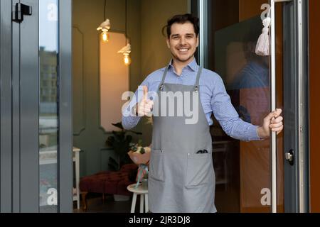 Der Besitzer eines gemütlichen Etablissement freundlich und herzlich trifft seine Kunden an der Schwelle des Etablissement, indem er die Tür öffnet Stockfoto