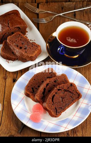 Hausgemachter Schokoladenkuchen mit rosa Bonbons und Tee in blauer Tasse verical geschnitten Stockfoto