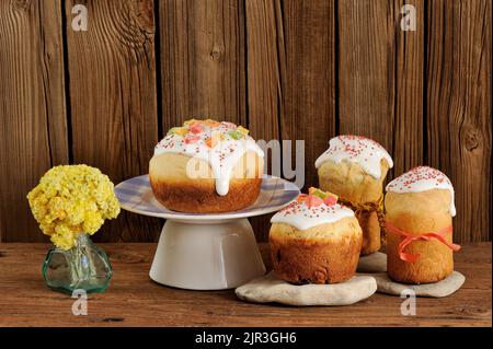 Kulich, russisches osternbrot mit Sahnehäubchen und kandierten Früchten mit gelben Blumen auf Holzgrund mit viel Platz Stockfoto