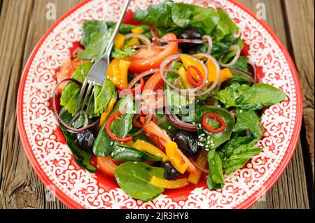 Heller Salat mit Gemüse: Spinat, Tomaten, Oliven, Zwiebel, Paprika in scharlachroten Teller Nahaufnahme Makro Stockfoto