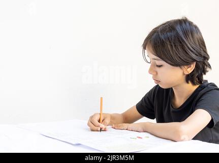 Junger ostasiatischer Teenager Junge studiert mit einem Stift und einem Notizbuch am Tisch schreiben. Der Junge, der zu Hause seine Schulaufgaben macht. Schwarzes T-Shirt Stockfoto