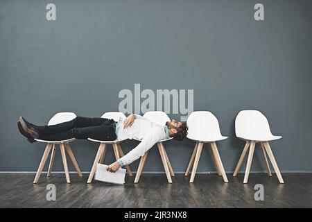 Kann dieses Warten nicht länger dauern? Ein junger Mann, der sich auf einer Reihe von Stühlen legt und in der Schlange auf ein Vorstellungsgespräch wartet. Stockfoto