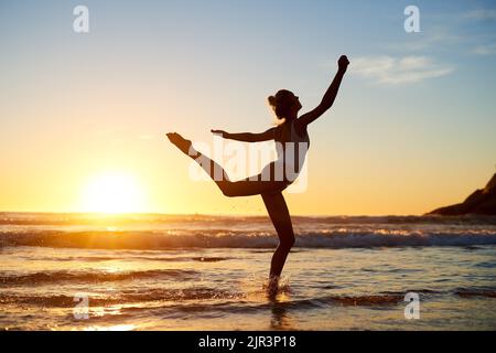 Eines Tages wird es sich lohnen. Silhouette einer jungen Frau gegen einen wunderschönen Sonnenuntergang am Strand. Stockfoto