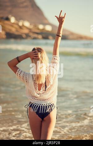 Halten Sie Ihren Geist salzig. Rückansicht einer jungen Frau am Strand mit der Hand in der Luft. Stockfoto